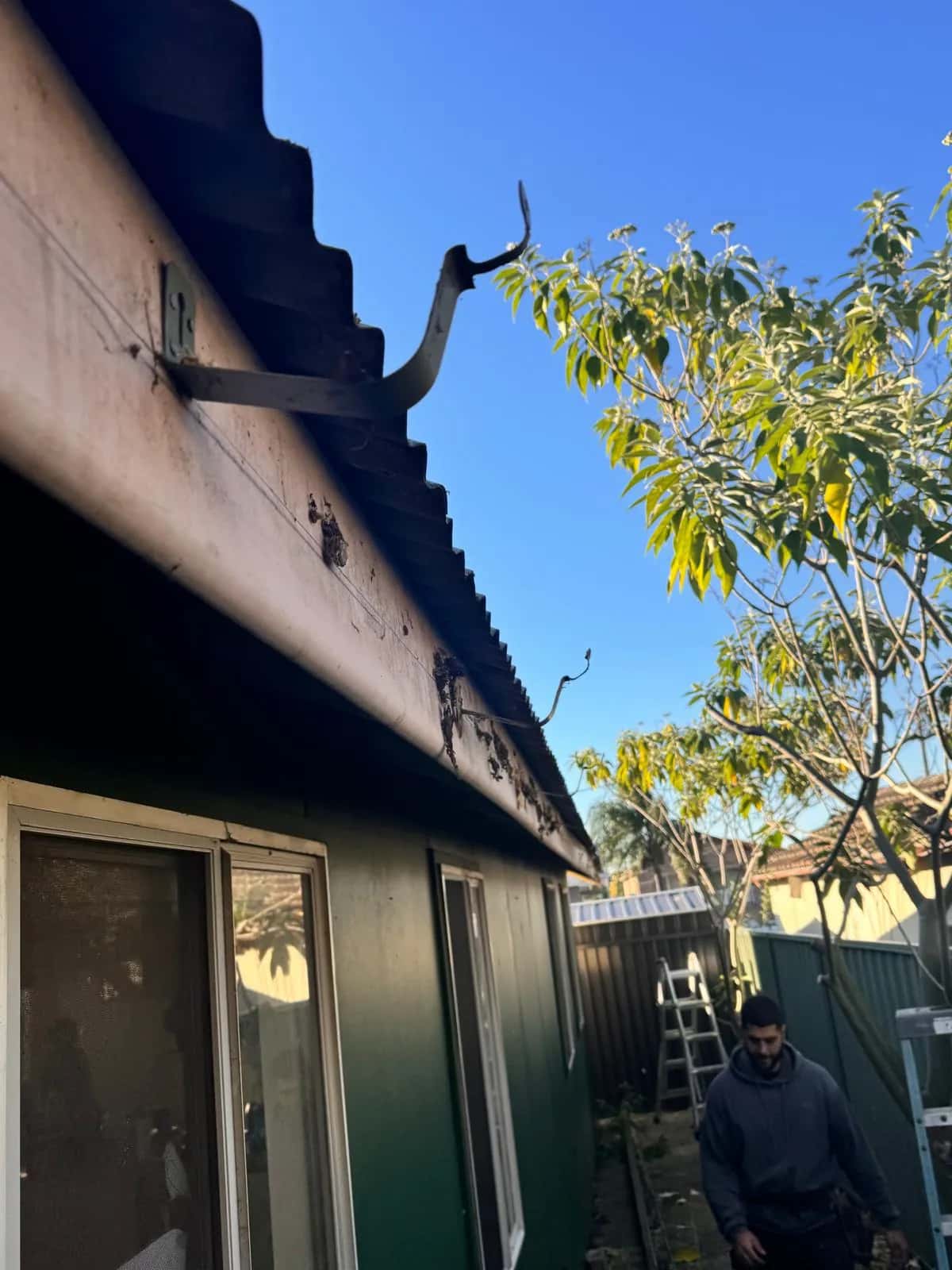 Rusted-through guttering along a Sydney roofline, with a Mr. Clog plumber below preparing to replace it