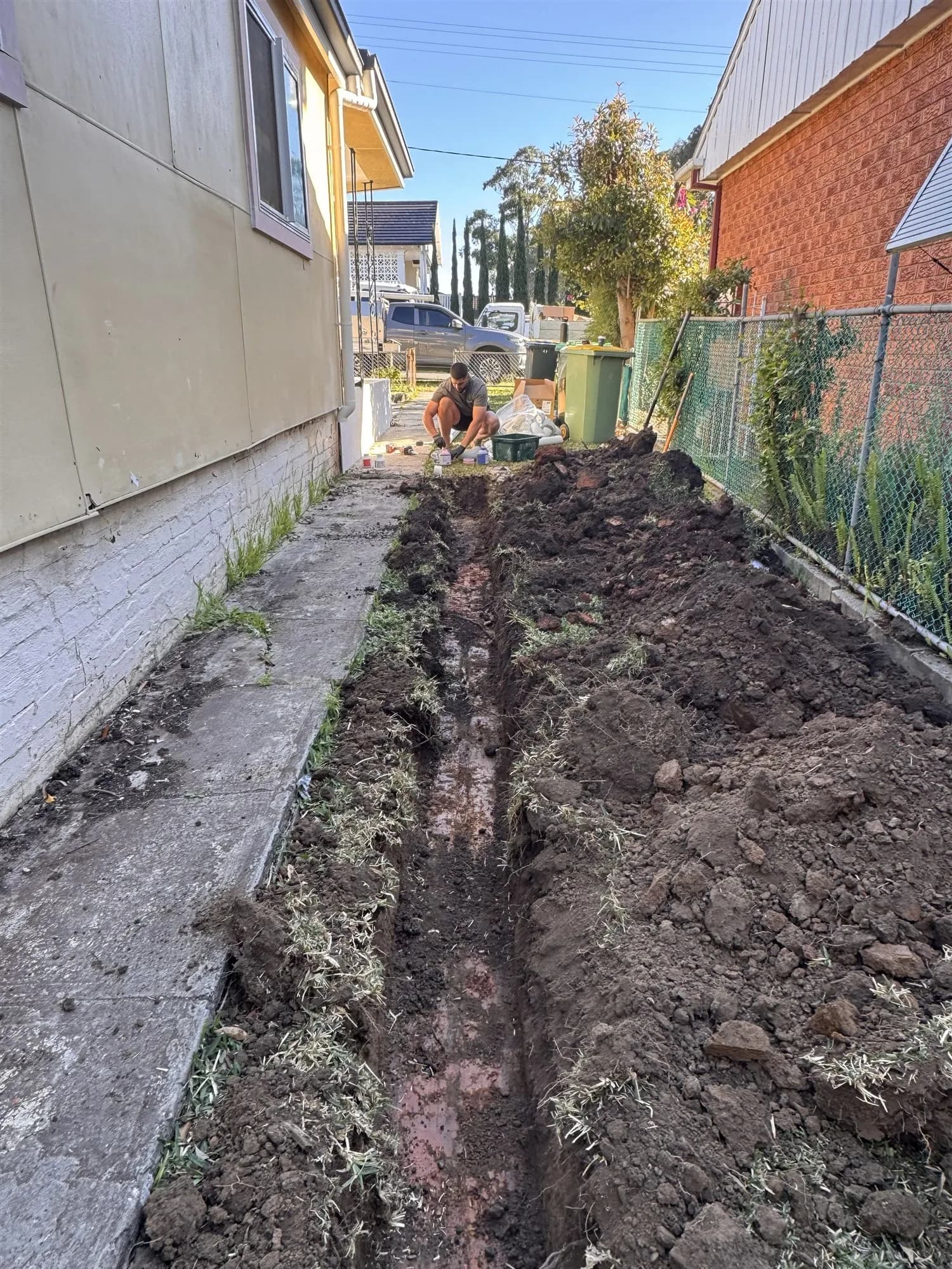 Trench dug by machine along the side of a house for a new stormwater line