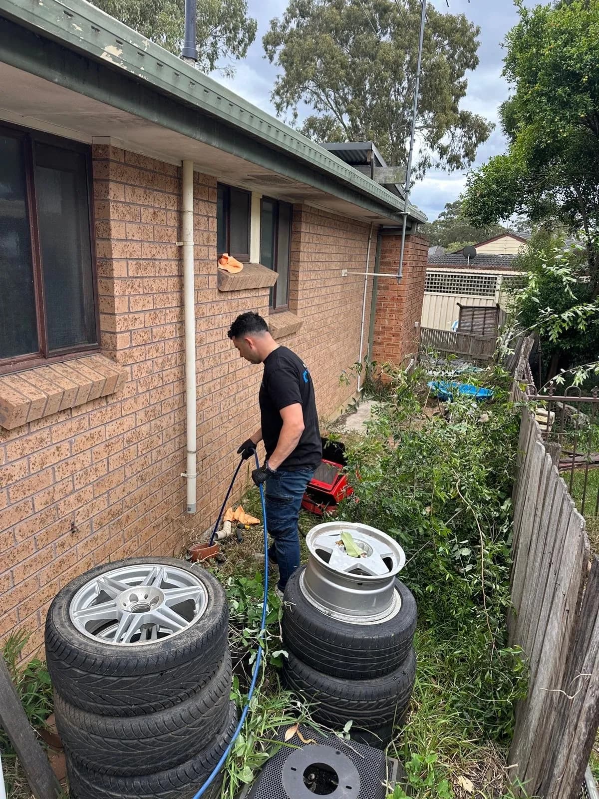 Mr Clog plumber jet blasting a blocked sewer beside a brick house