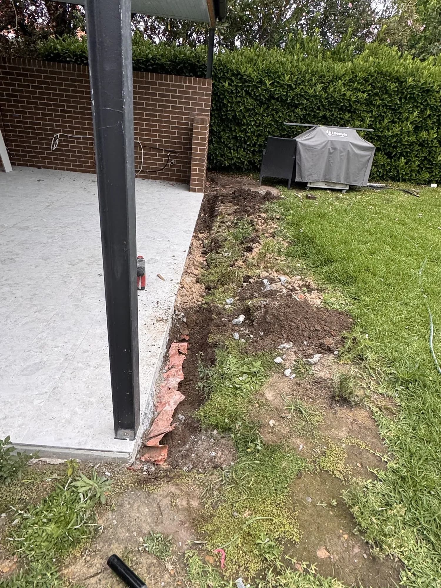 Trench dug along the edge of a new tiled outdoor area before the strip drain went in