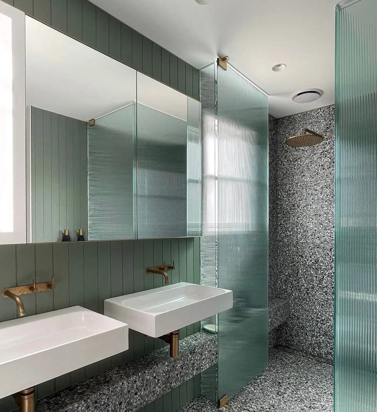 Green bathroom with terrazzo, twin wall-hung basins and brass wall-mounted tapware