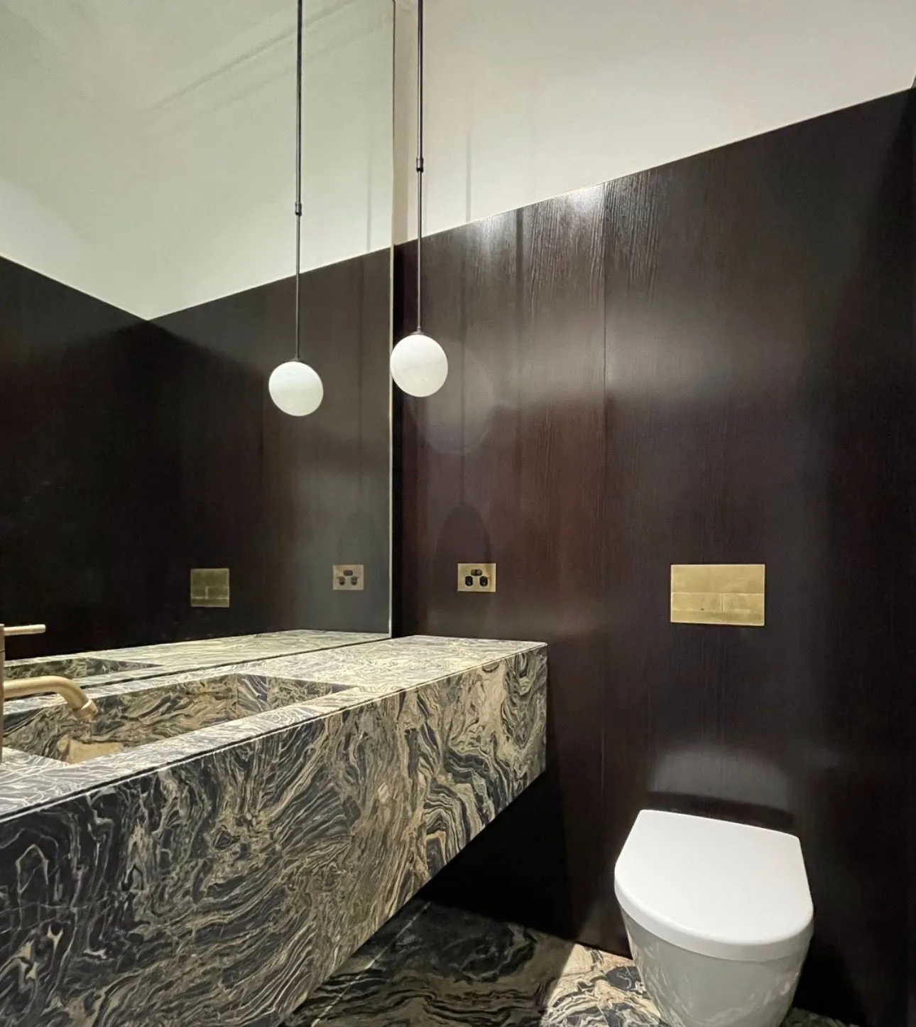 Powder room with a marble vanity, wall-mounted brass tapware and a wall-hung toilet