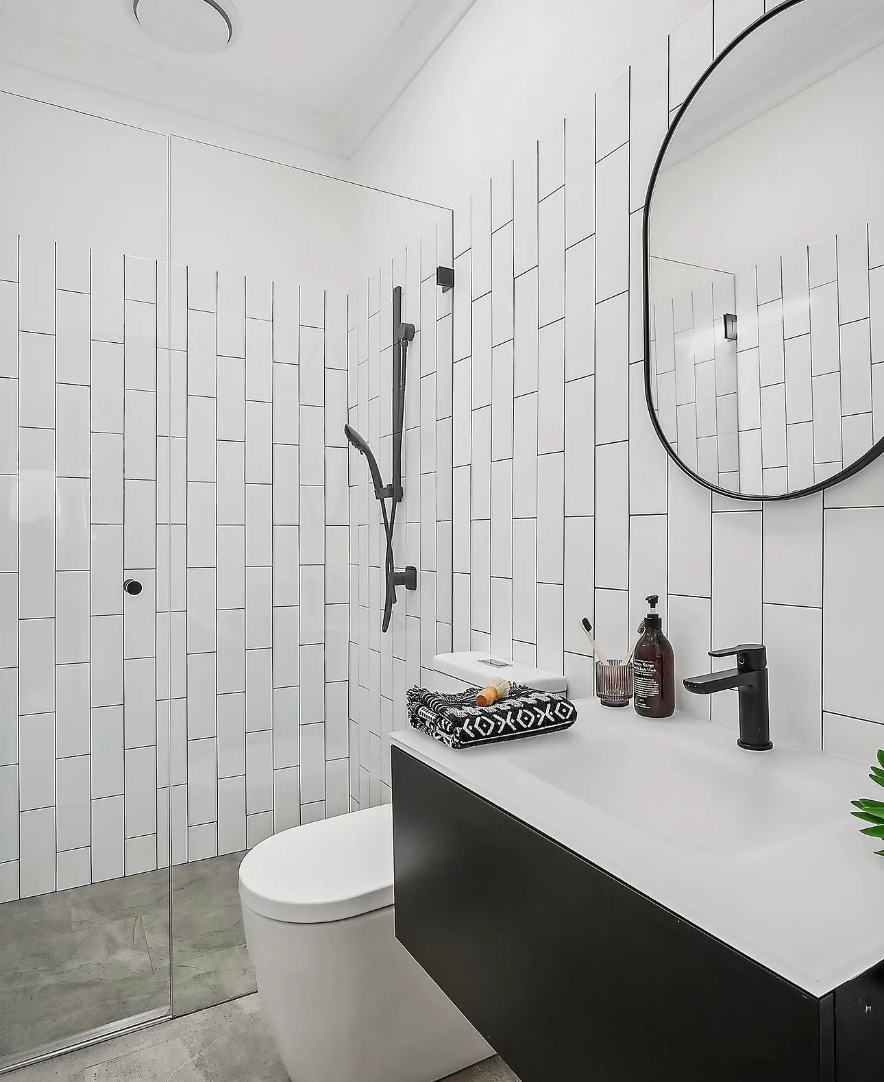 White bathroom with vertical tiles, black shower rail and black basin mixer