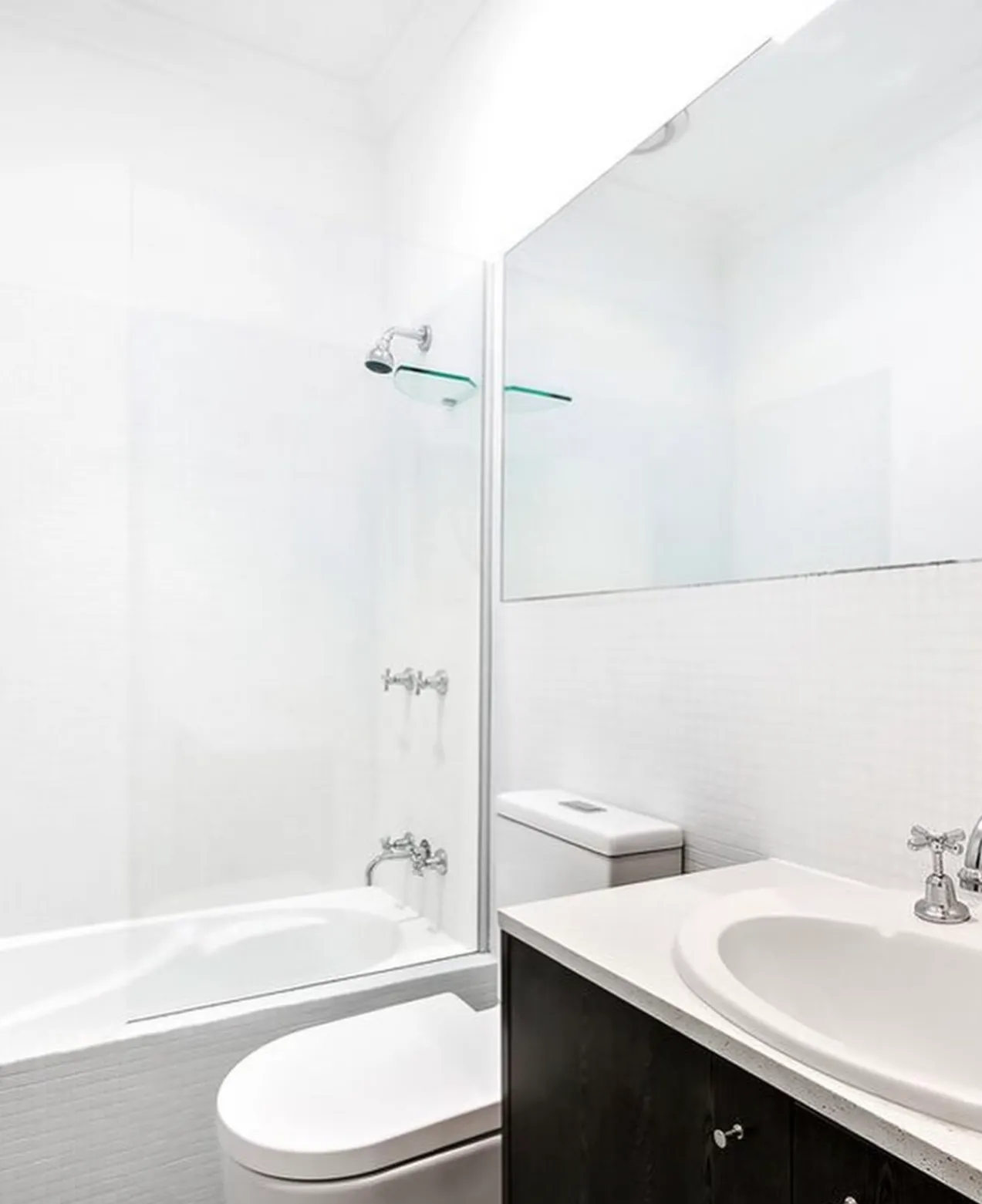 White bathroom with a shower over the bath, glass screen and vanity