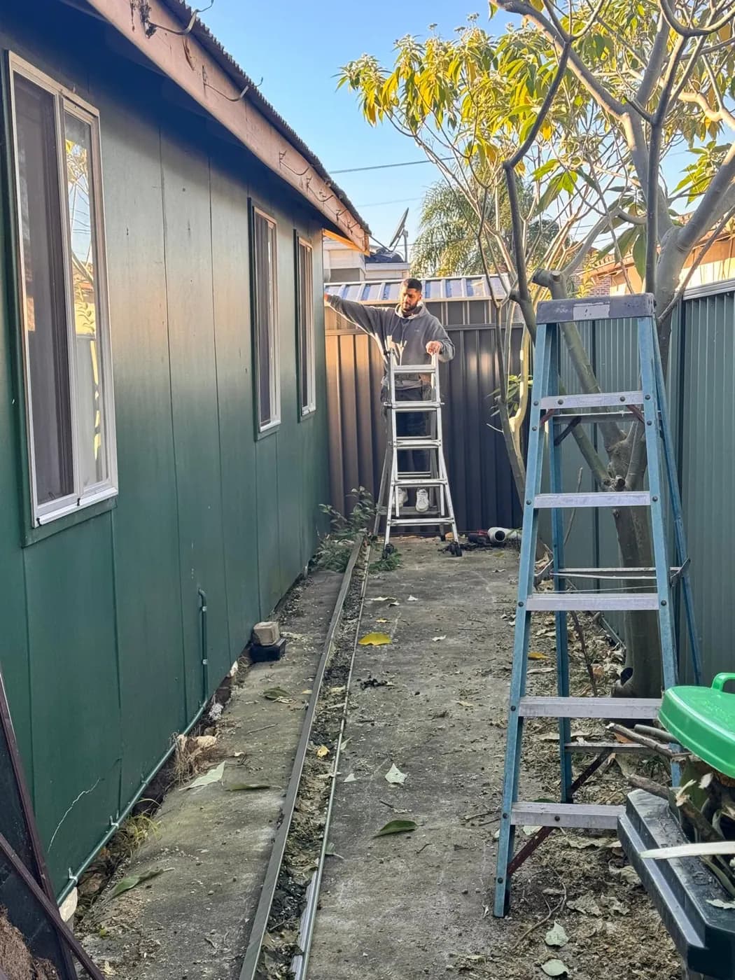 Mr. Clog plumber on a ladder in a narrow side passage fixing the new gutter length into place along the roofline