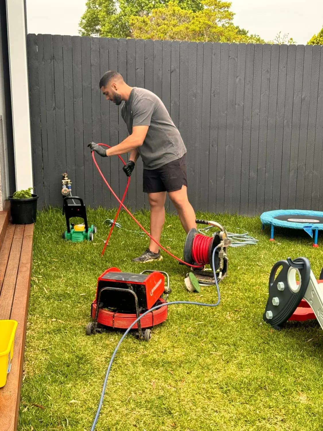 Mr. Clog plumber running a high-pressure jetter hose into a backyard drain at a Sydney family home