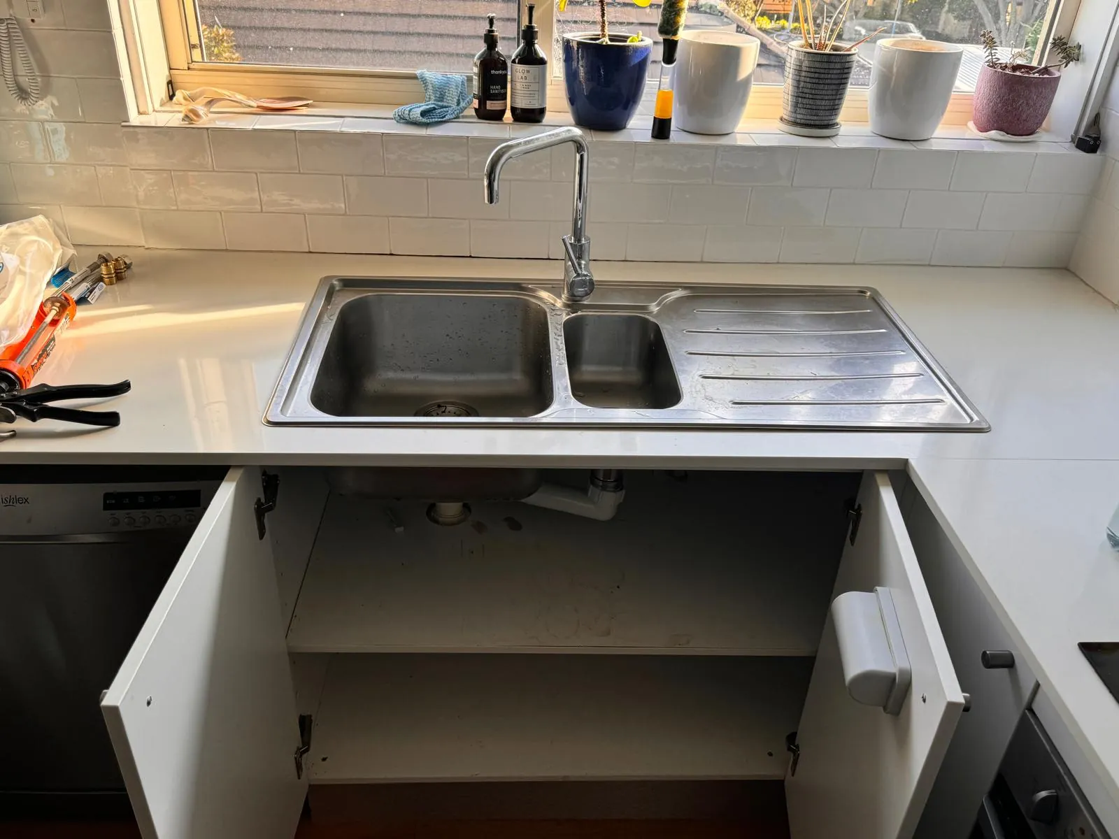 Original drop-in stainless kitchen sink with a drainer board and plain mixer tap, cupboard below open ready for removal