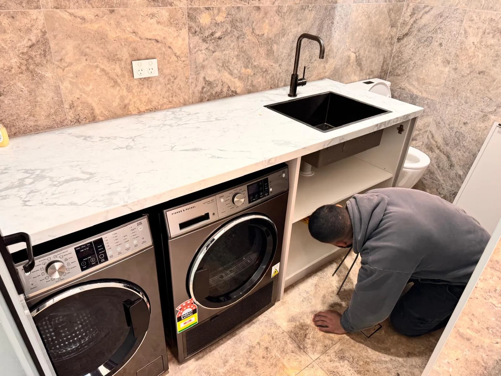 Mr. Clog plumber connecting the waste under a new laundry benchtop, with washer, dryer and a black undermount sink installed
