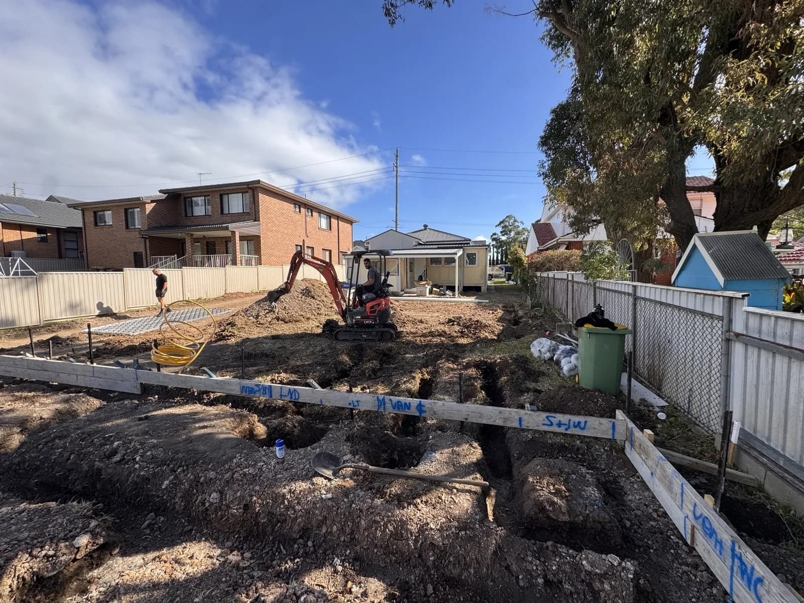 Excavator trenching in a backyard for a new granny flat's sewer drainage