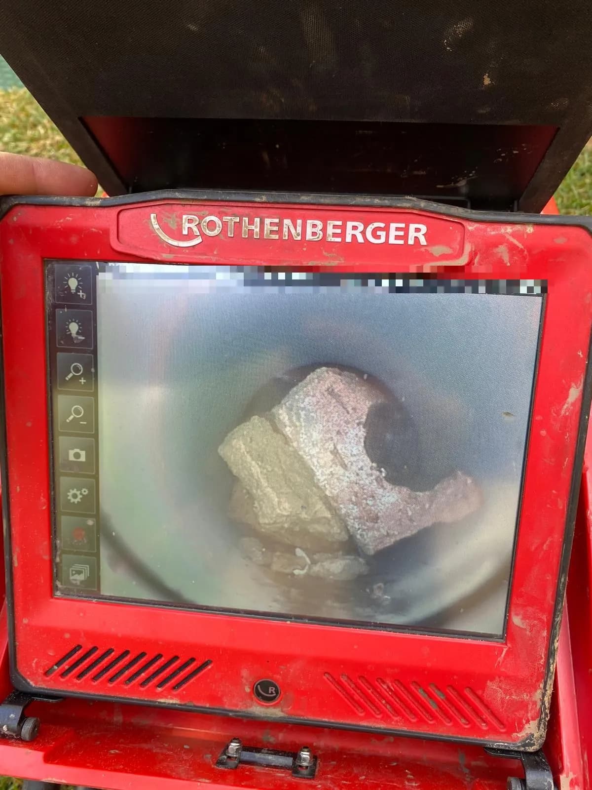 CCTV camera screen showing broken bricks and debris lodged inside a sewer pipe