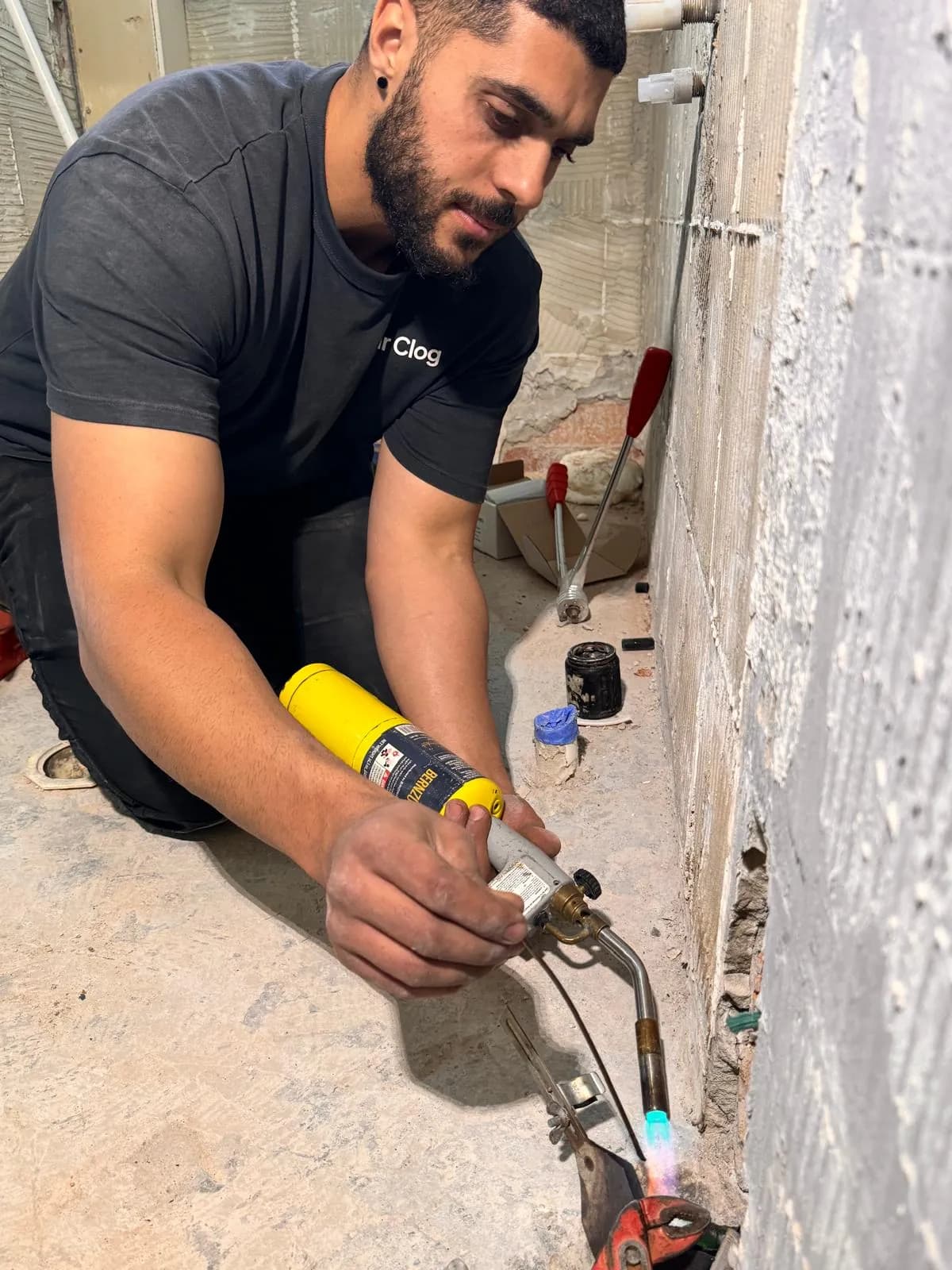 Mr. Clog plumber soldering a repair to a water pipe broken in a wall during a bathroom demolition