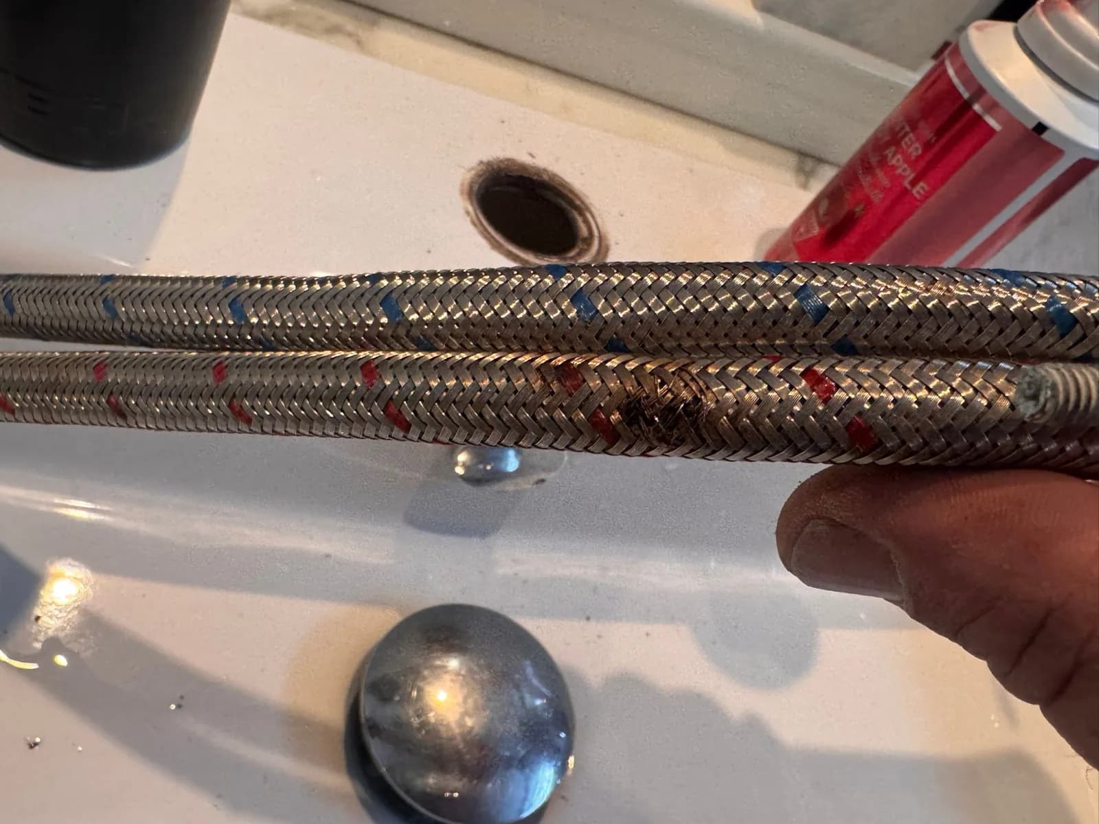 Close-up of a braided flexible tap hose with the stainless braid frayed and broken at the failure point