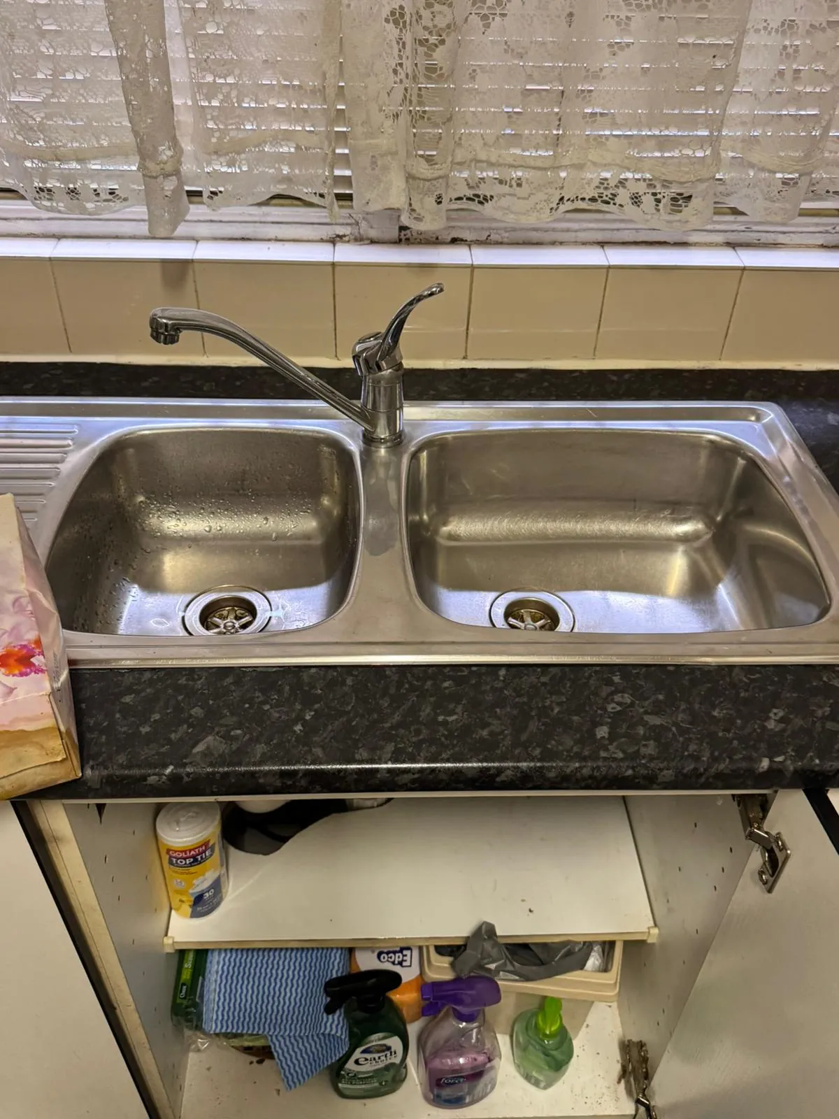 Worn chrome swan-neck kitchen mixer tap on an existing double-bowl sink