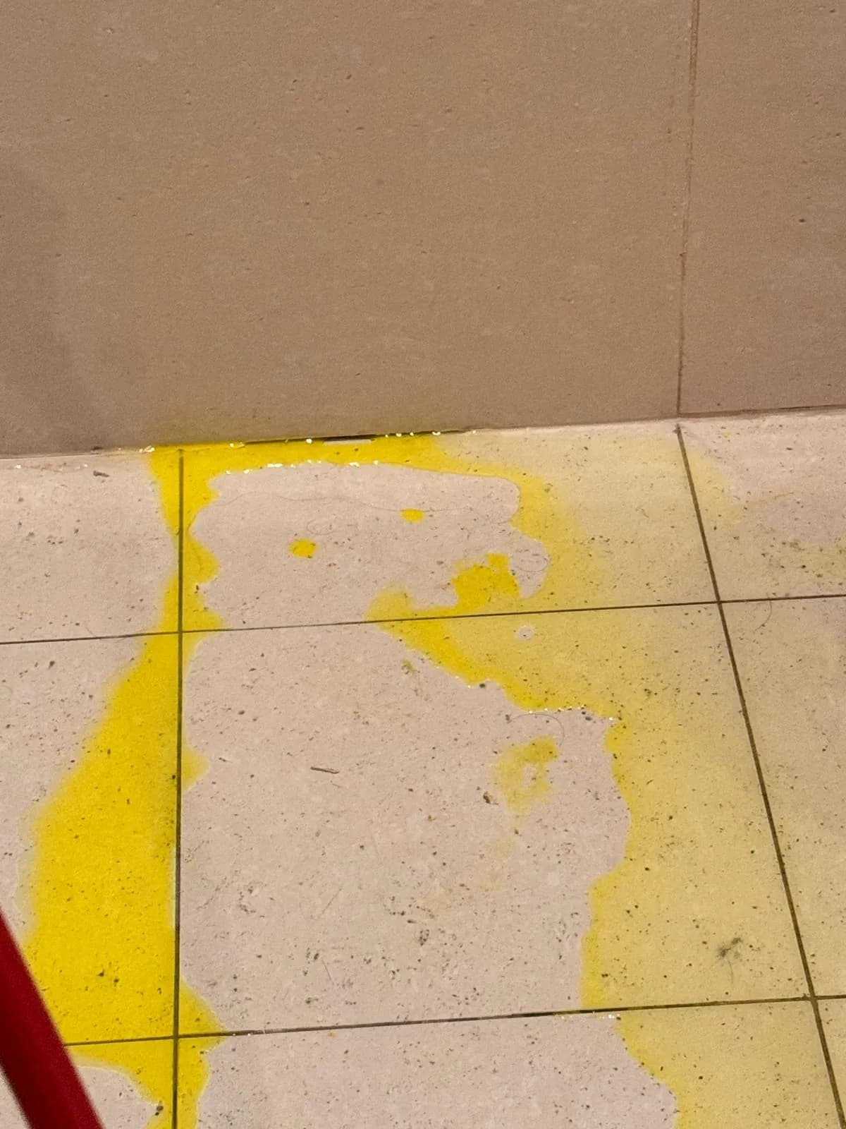 Yellow tracer dye seeping up through the grout lines of a tiled bathroom floor, marking the path of a hidden leak