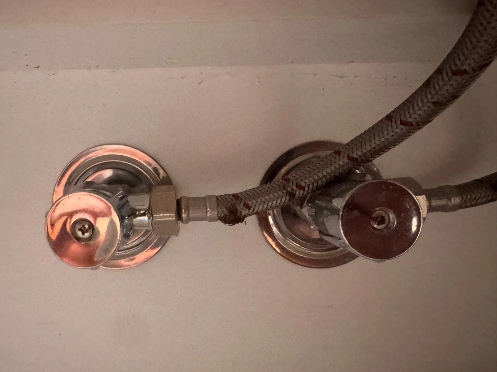 Braided flexi hose connected to a chrome under-sink isolation valve, with the braid frayed and broken just past the crimped fitting